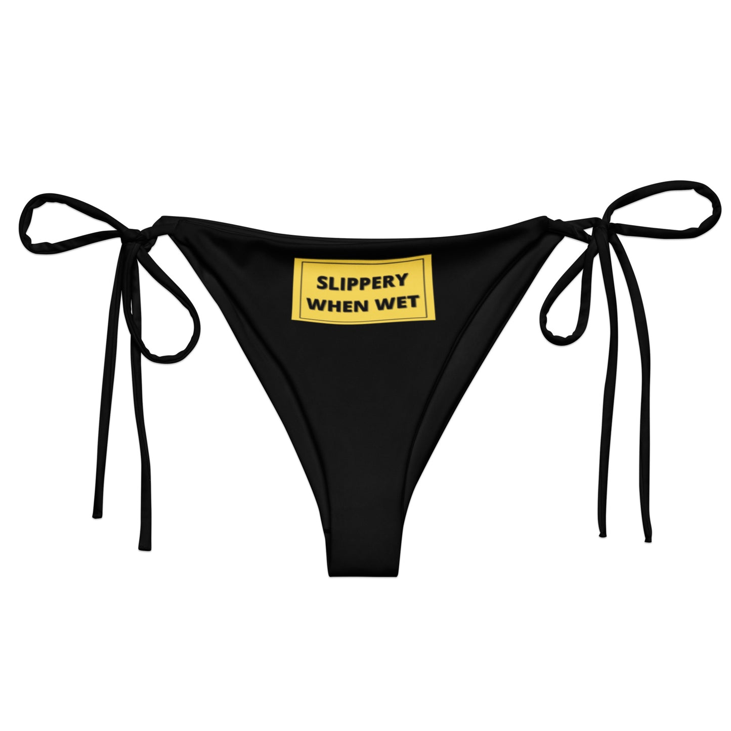 A black bikini bottom from Sensual Muse with a yellow sign on the front. The sign on the front says 'Slippery When Wet'. It has black writing in a yellow box.